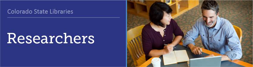 Researchers - Two library professionals sitting at a table with a laptop, book, and coffee, talking.