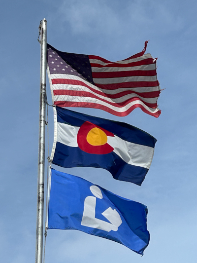 Flagpole outside of the Hayden Public Library, including a national library symbol flag, American flag, and Colorado flag